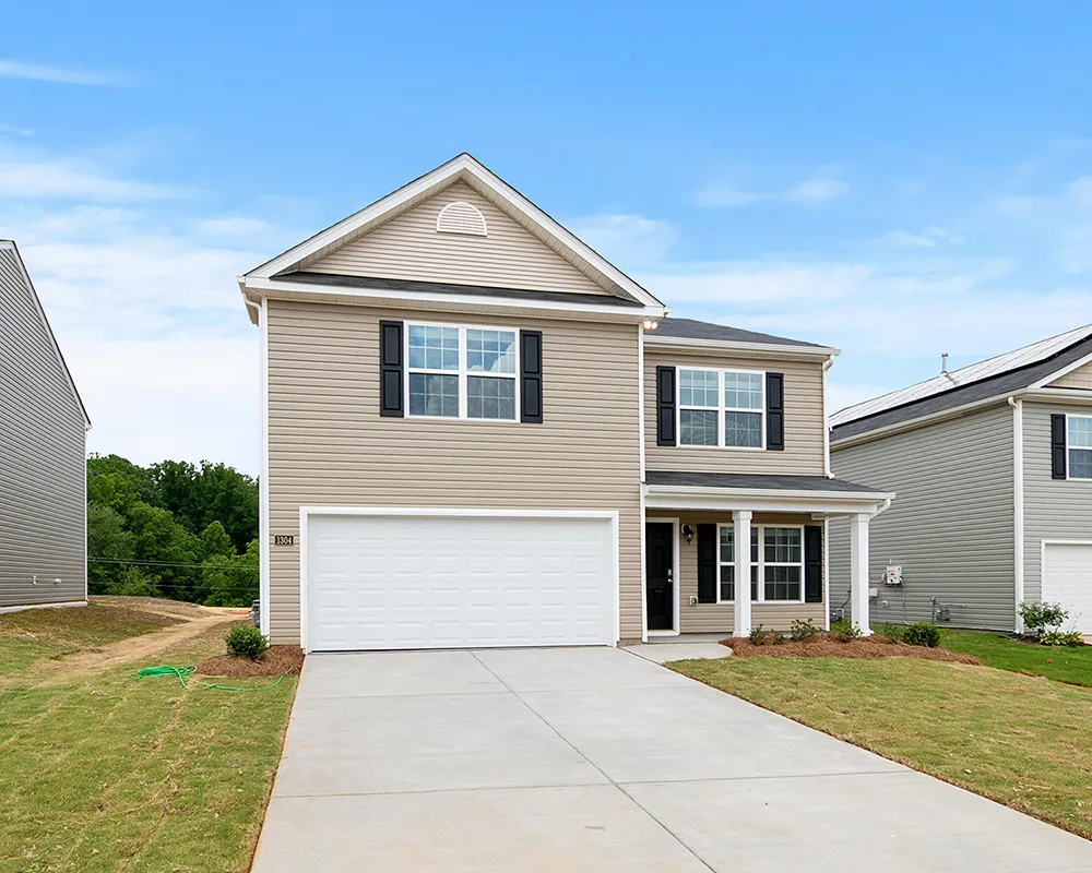Two-story suburban house with beige siding, a double garage, and a driveway in a newly built residential neighborhood.